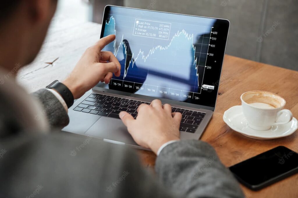 A person analyzing stock trends on a laptop with a coffee cup nearby