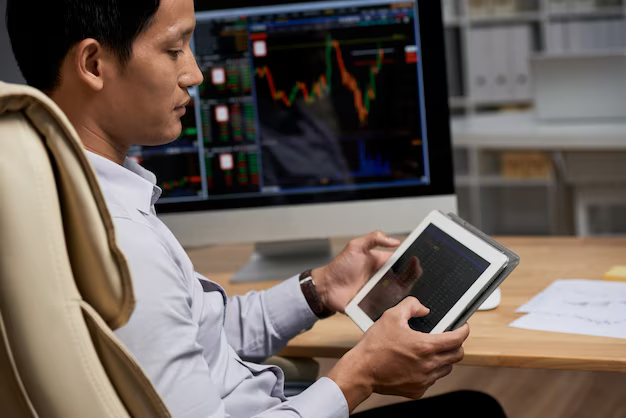 A man holds a tablet in his hands against the background of a computer with a graph