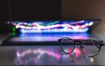 Glasses in focus before an out-of-focus laptop with colorful keyboard lighting