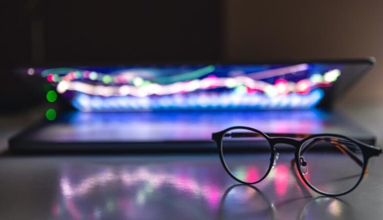 Glasses in focus before an out-of-focus laptop with colorful keyboard lighting