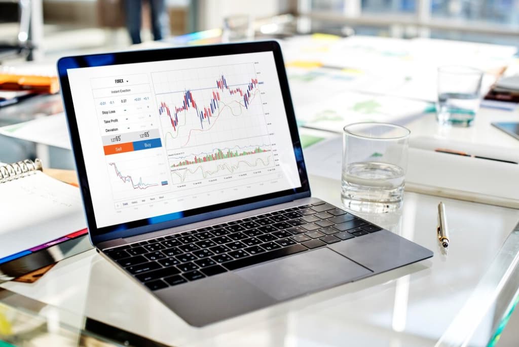 A laptop on a desk displays complex financial charts