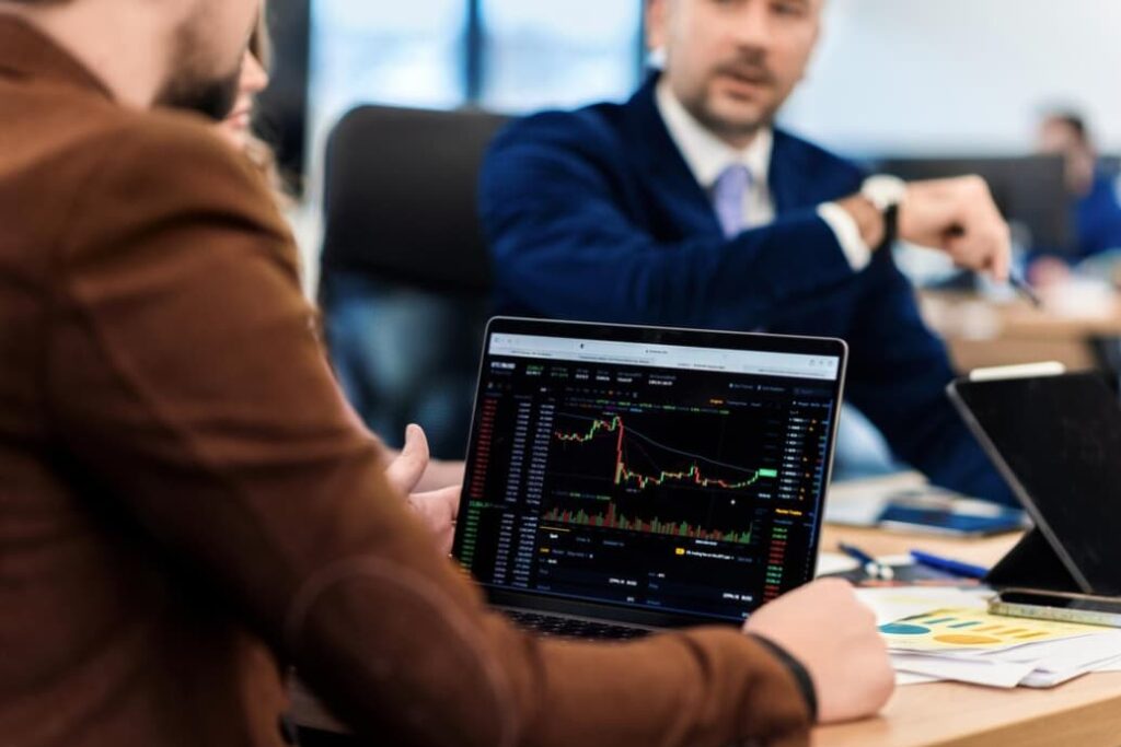 Two professionals discuss over a laptop displaying financial charts